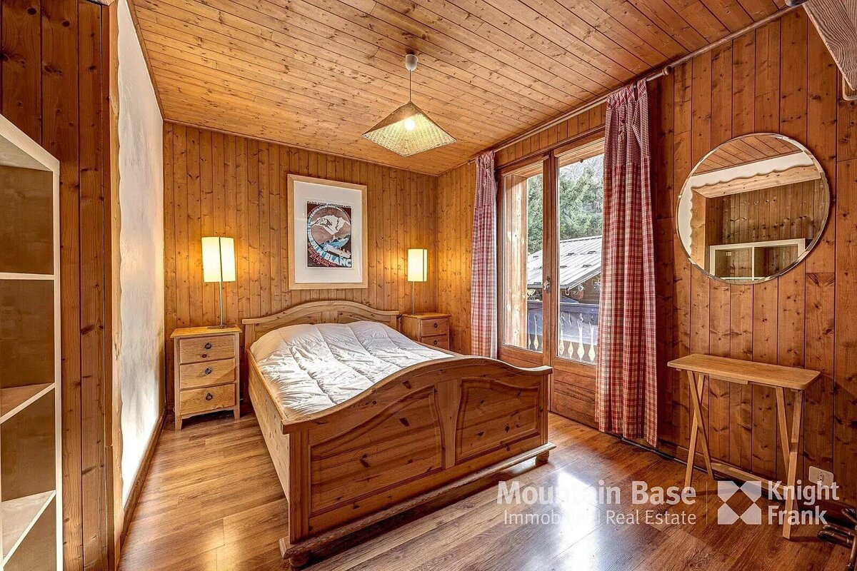 A bedroom with wood paneling and a bed and a mirror from mountain base