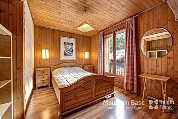 A bedroom with wood paneling and a bed and a mirror from mountain base