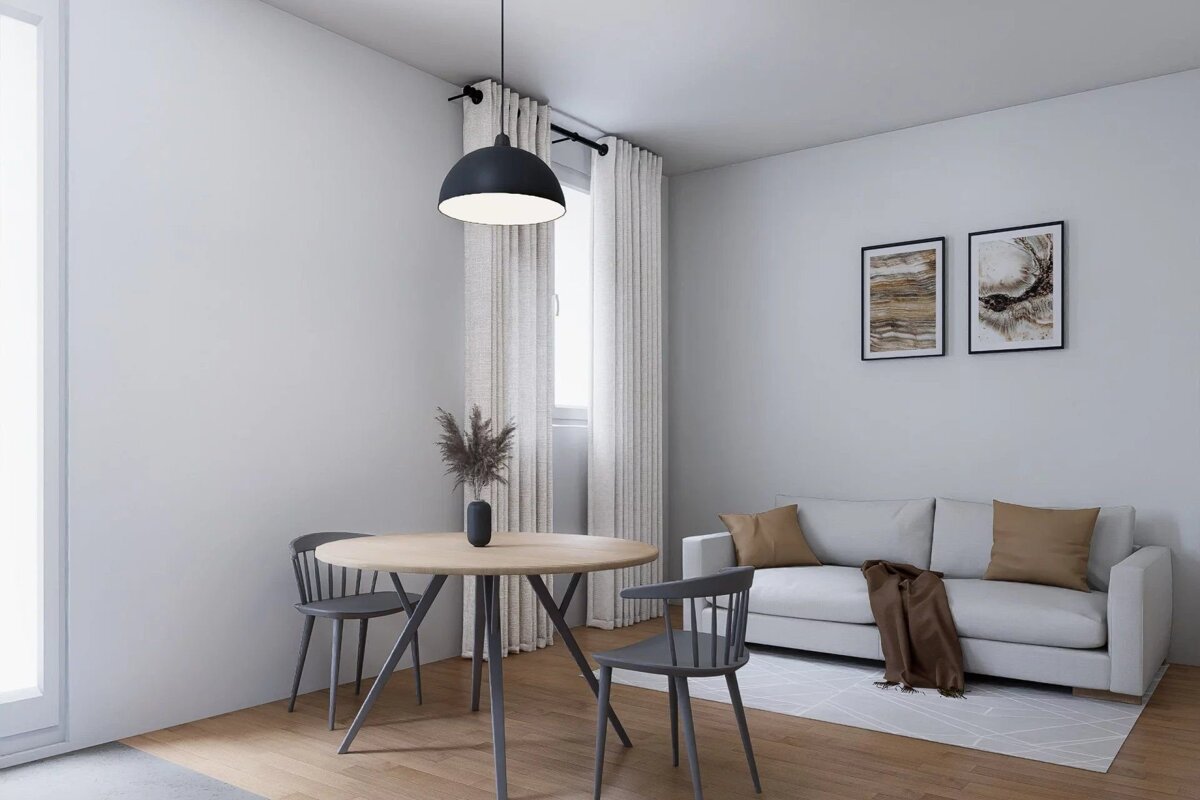 Minimalist living area featuring a round dining table, grey chairs, and a white sofa with brown pillows in a neutrally decorated room.