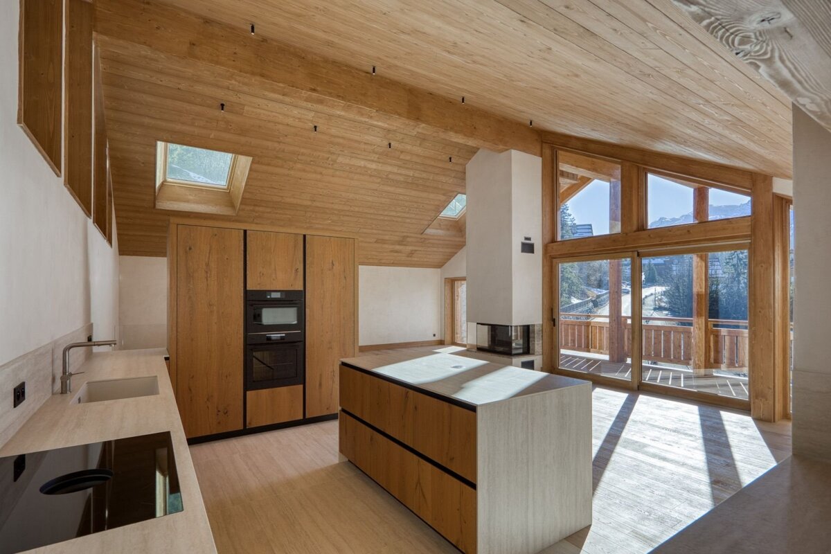 A modern wood kitchen with an island, integrated appliances, a fireplace, and large windows offering a mountain view. Skylights provide natural light.