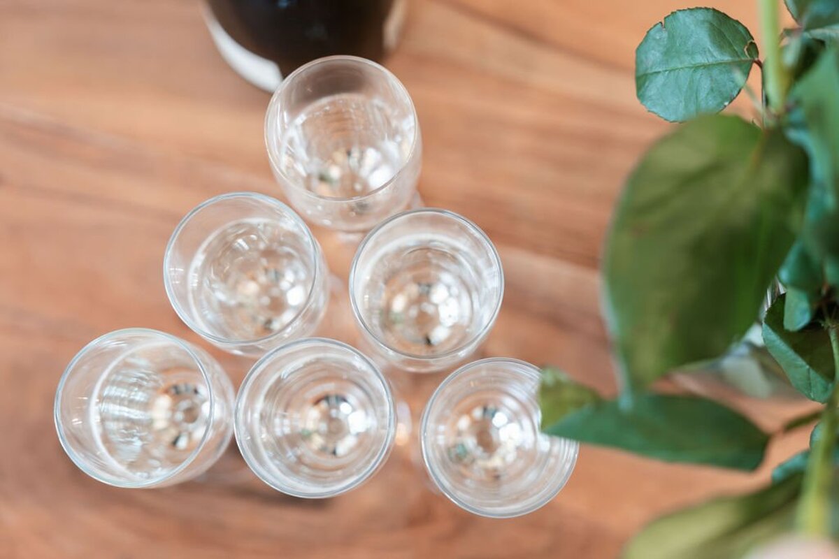 Top-down view of six champagne glasses arranged in a triangle on a wooden table, with green leaves nearby.