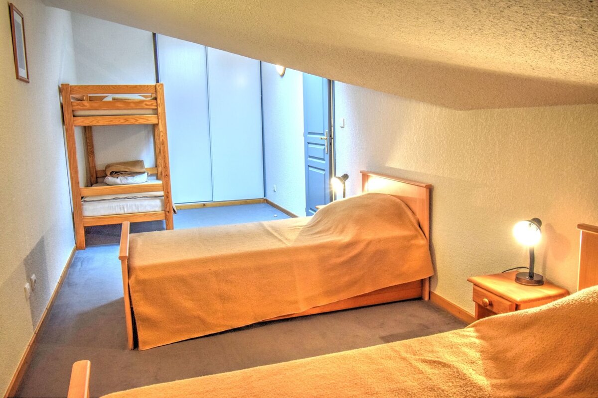 Attic bedroom with a wooden bunk bed, two single beds with orange blankets, nightstands with lamps, white closets, and a blue door.