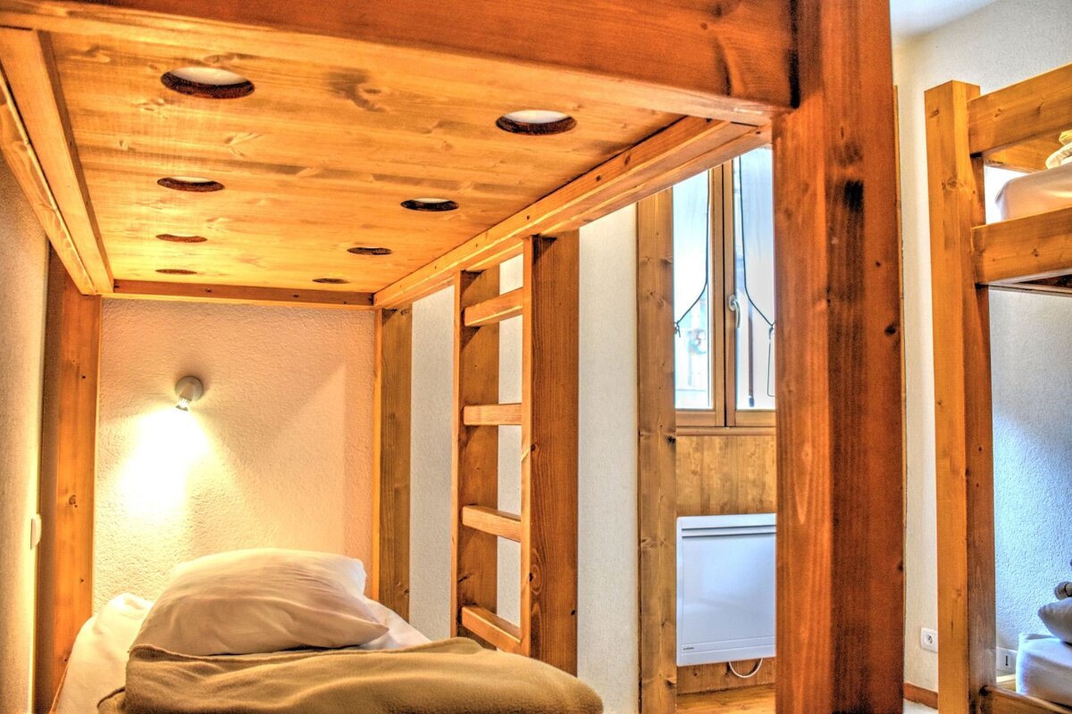 A cozy room featuring sturdy wooden bunk beds with built-in ladders and a warm reading light near the bottom bunk.