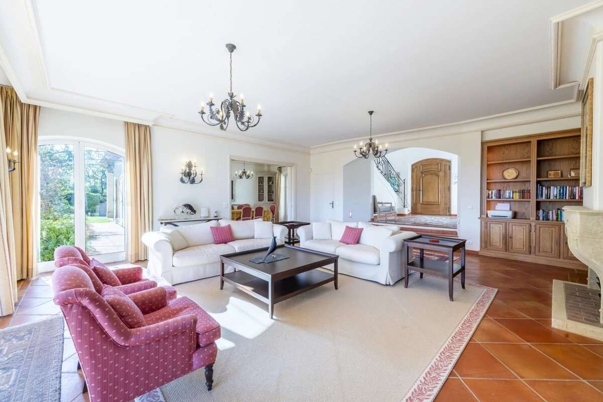 Spacious living room with white sofas, pink armchairs, a dark wood coffee table, terracotta tiles, and two chandeliers.