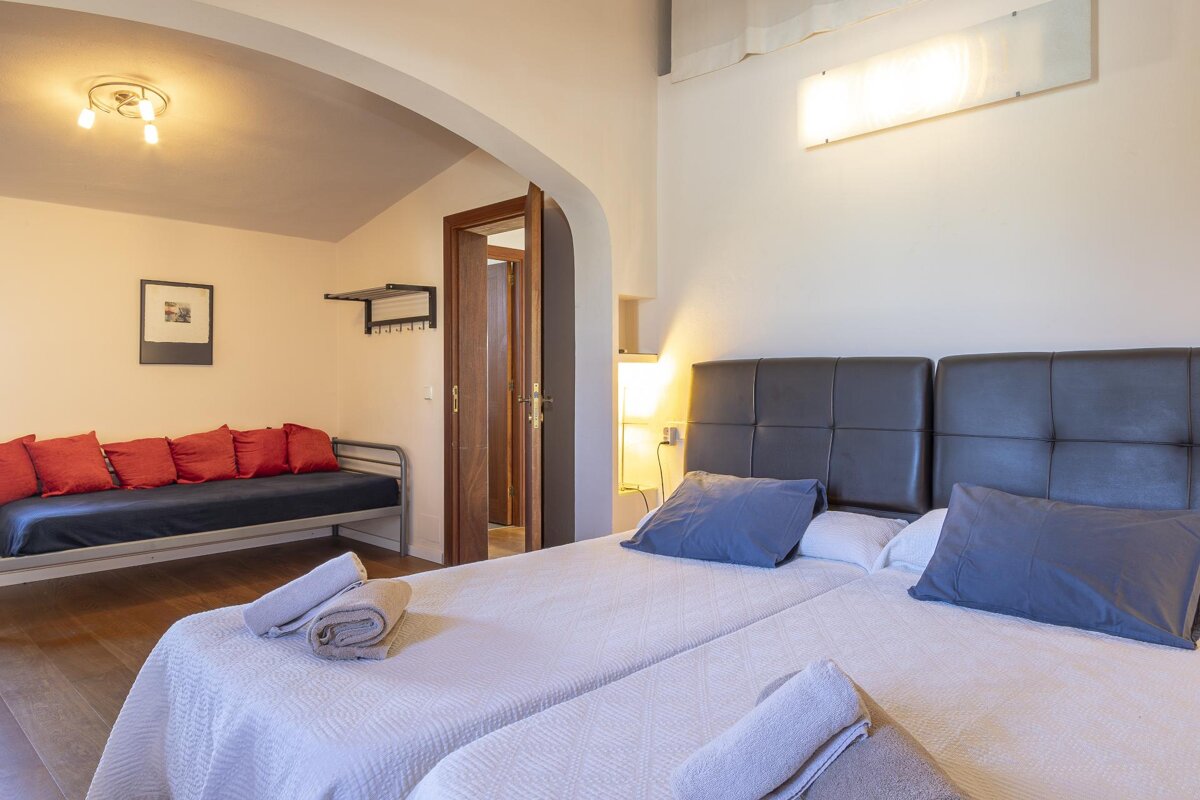 A bedroom with two beds and a couch with red pillows