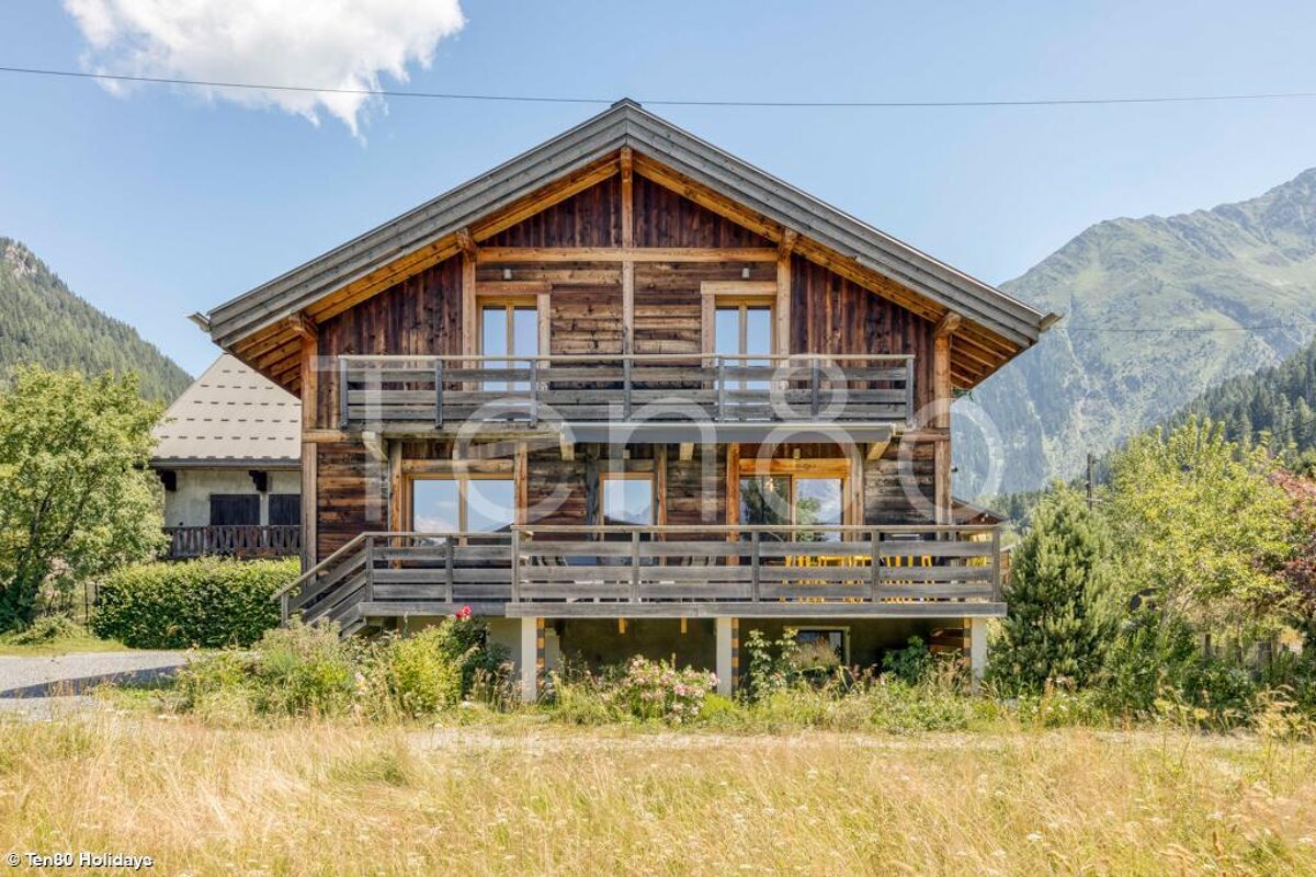 A large wooden house with a balcony and mountains in the background