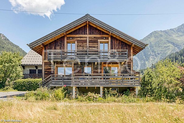 A large wooden house with a balcony and mountains in the background