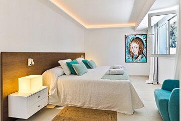 A bedroom with a painting on the wall above the bed