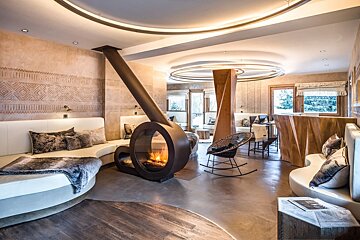 A chic modern lounge featuring a distinctive circular fireplace, curved seating, textured walls, and ambient circular ceiling lights.