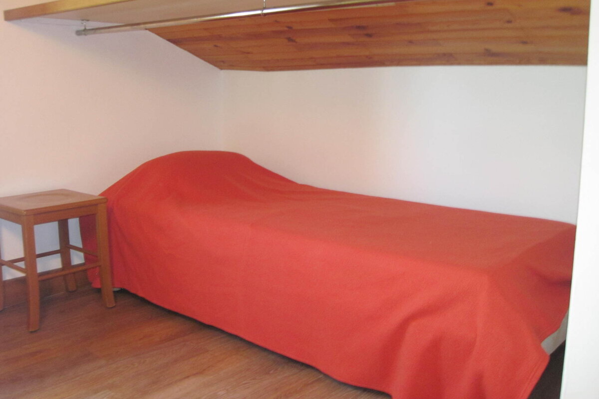 A small bedroom with a single bed and a wooden stool
