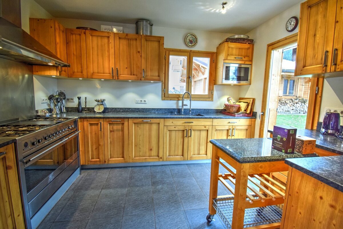 A warm kitchen with light wood cabinets, dark granite countertops, stainless steel appliances including a large range, and a door to a grassy yard.