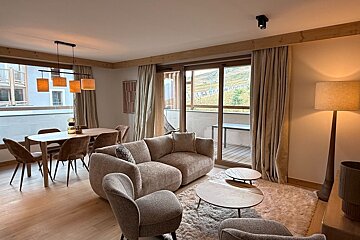 Cozy modern living room with beige seating, a dining set, plush rug, and large sliding glass doors leading to a balcony.