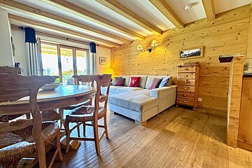 Cozy alpine cabin interior featuring a wooden dining set, a grey sectional sofa, and warm wood-paneled walls and ceilings.
