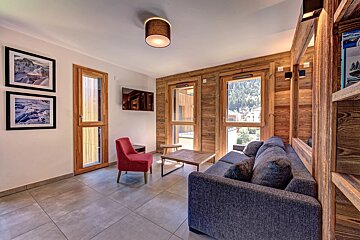 Cozy modern alpine living room with a grey sofa, red armchair, wood-paneled walls, and tiled flooring.