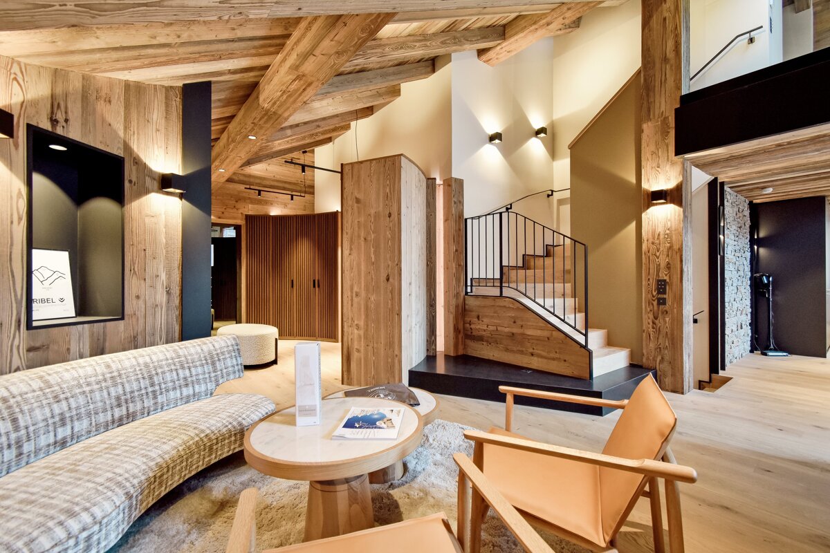 Warm, modern rustic chalet interior with extensive wood paneling, exposed beams, a comfortable seating area, and an inviting staircase.