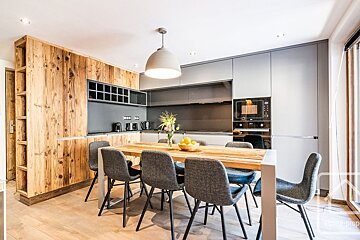 A modern kitchen and dining area features rustic wood paneling, sleek gray cabinetry, a wooden dining table with gray chairs, and contemporary appliances.