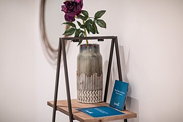A vase with a purple flower in it sits on a shelf