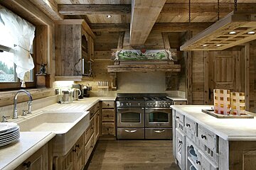 Cozy, rustic kitchen made almost entirely of wood, with a large farmhouse sink, stainless steel range, and decorative range hood.