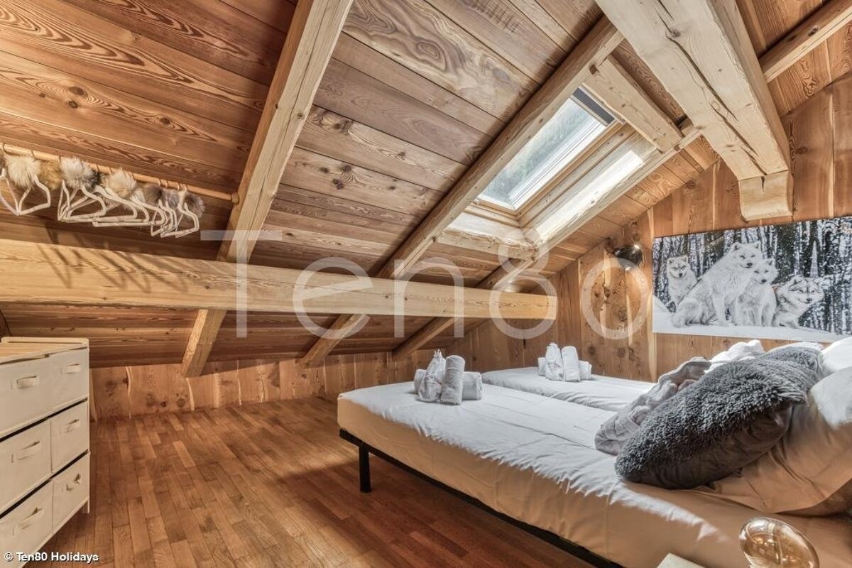Cozy wooden attic bedroom with two single beds, a skylight, exposed beams, and rustic wood-paneled walls and ceiling.