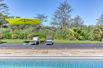 A green umbrella sits on a deck next to a swimming pool