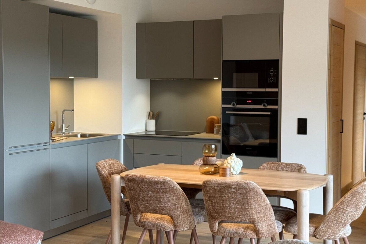 Modern gray kitchen with built-in appliances and a wooden dining table set with textured brown chairs.