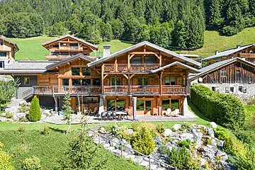 A large wooden house sits in the middle of a lush green field