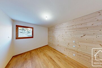 Empty room with light wooden floor & wall paneling. White walls, wood-framed window overlooks a snowy scene.
