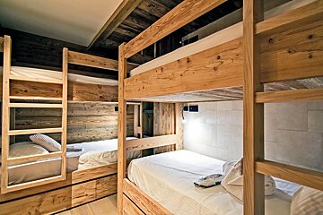 Cozy chalet-style room with multiple rustic wooden bunk beds, fresh white bedding, and wood-paneled walls/ceiling for a warm sleeping space.