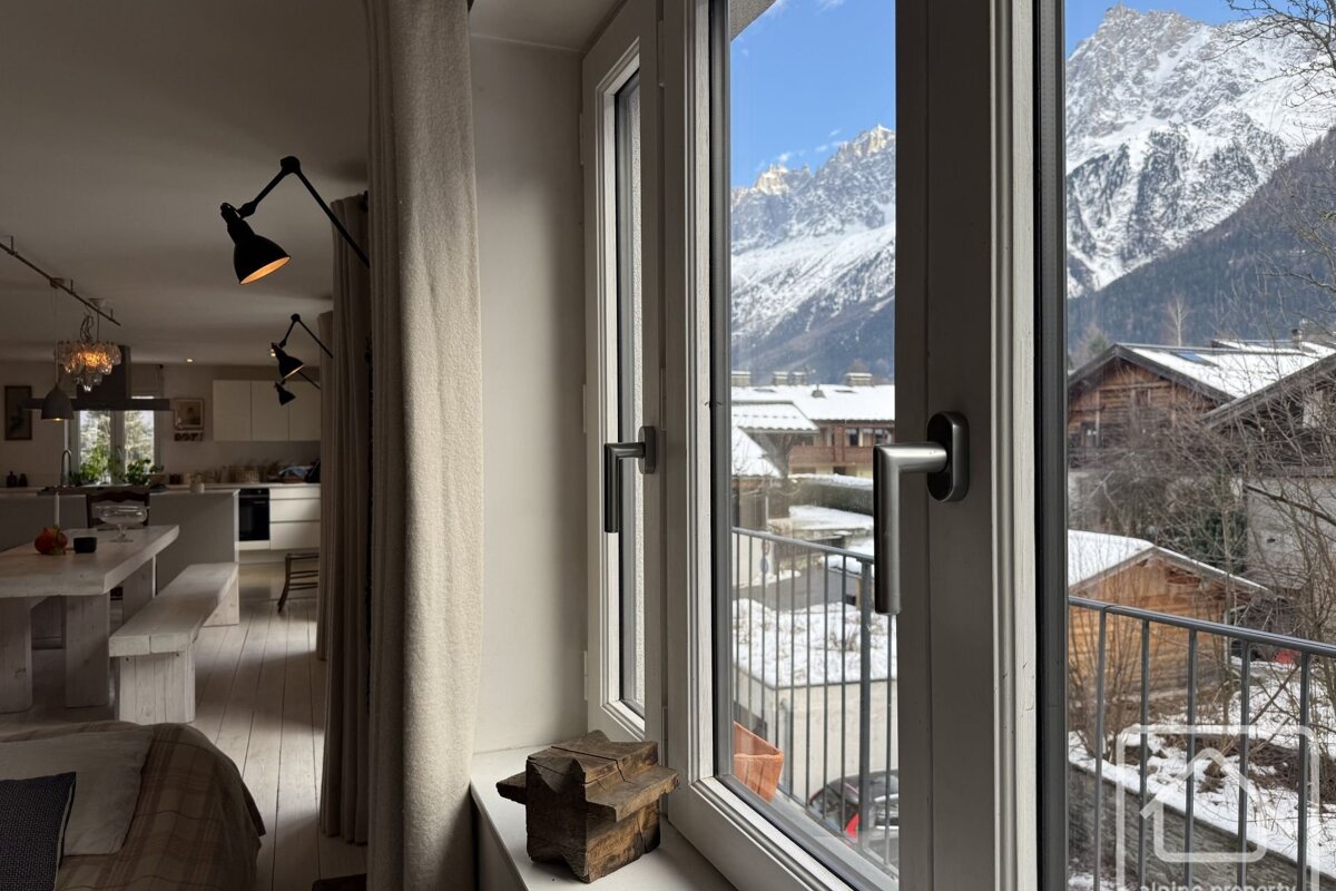 An alpine apartment interior with a large window looking out at snow-covered mountains and chalets.