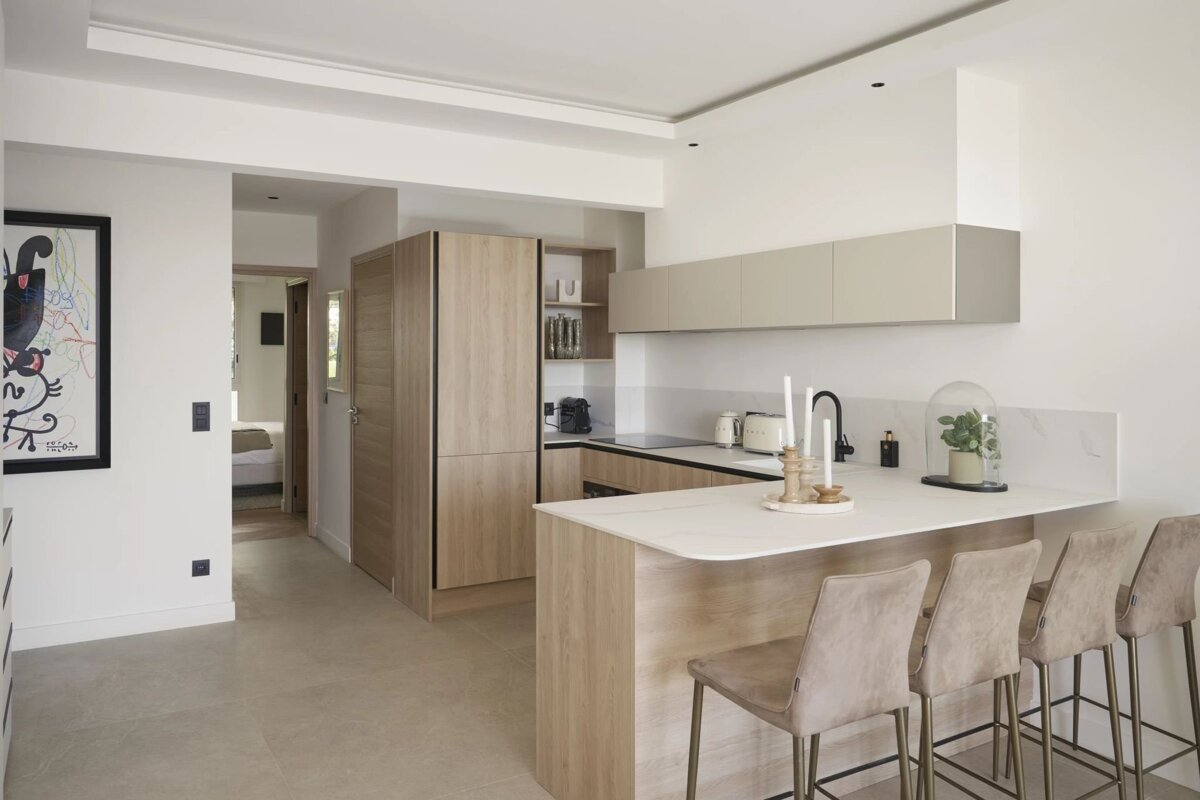 Minimalist kitchen featuring light wood cabinets, a white counter island with four beige bar stools, and bright, modern decor.