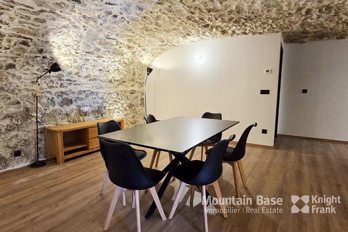 Modern dining area featuring a black table and chairs under a rustic vaulted stone ceiling.