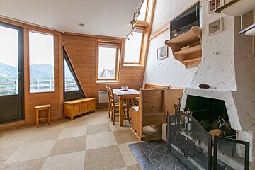 Cozy, rustic room with wood paneling, a dining area, and fireplace. Large windows offer mountain views. Features a checkered floor and slanted ceilings.