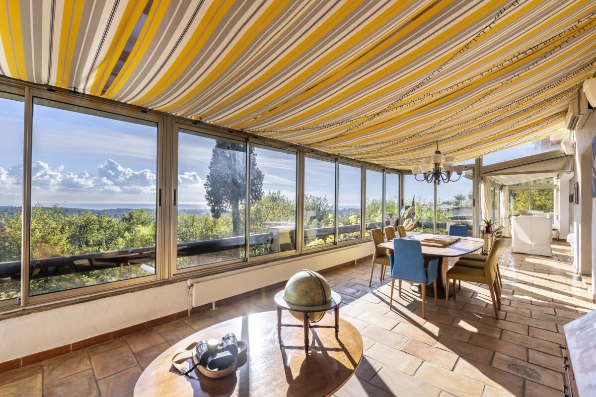 Bright sunroom with a yellow striped ceiling, large windows looking out over a green landscape, and a dining table set.