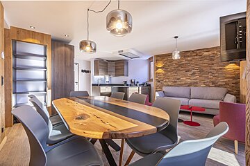 Modern open-plan apartment featuring a wood and resin dining table with grey chairs, leading into a living area with a wood accent wall.