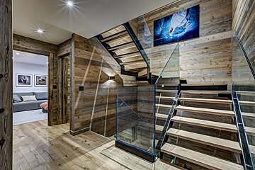 A wooden staircase with a glass railing and a picture on the wall above it