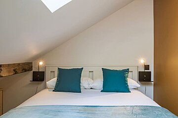 A bed with blue pillows and a skylight above it