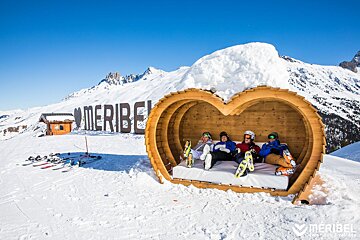 A group of people sitting in a heart shaped wooden structure with the word meribel in the background