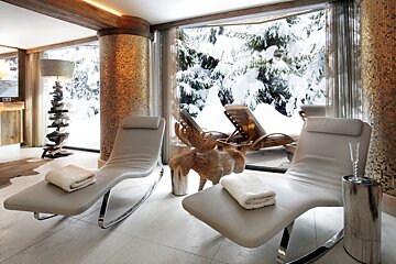 A luxurious relaxation room with lounge chairs and a golden moose, offering a stunning panoramic view of a snow-covered winter forest.