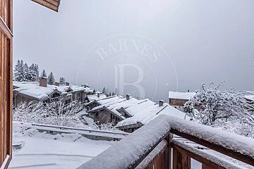 A snow-covered balcony overlooks winter chalets nestled in a foggy mountain village.