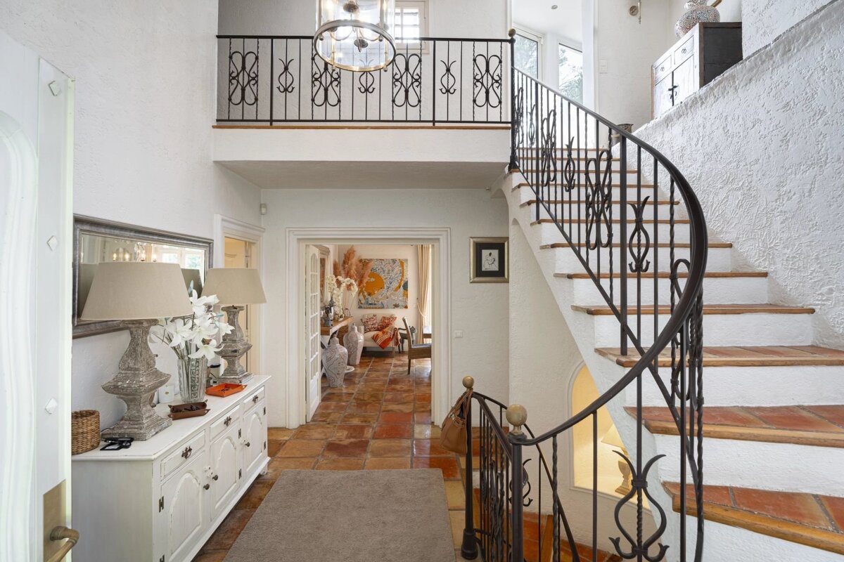 Bright Mediterranean entryway with terracotta tile floors, a white console table, and a winding staircase with wrought-iron railings.
