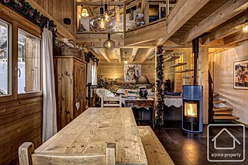 Cozy wooden cabin interior featuring a rustic dining table, a glowing fireplace, a warm living area, and a loft overhead.