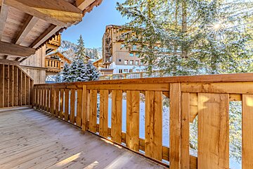 Wooden balcony overlooking a sunny, snowy mountain village with frosted trees and rustic chalet buildings.