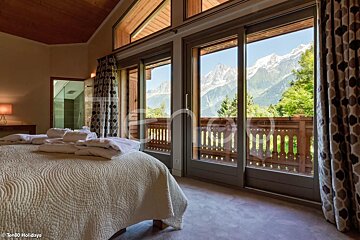 A bedroom with a balcony and mountains in the background