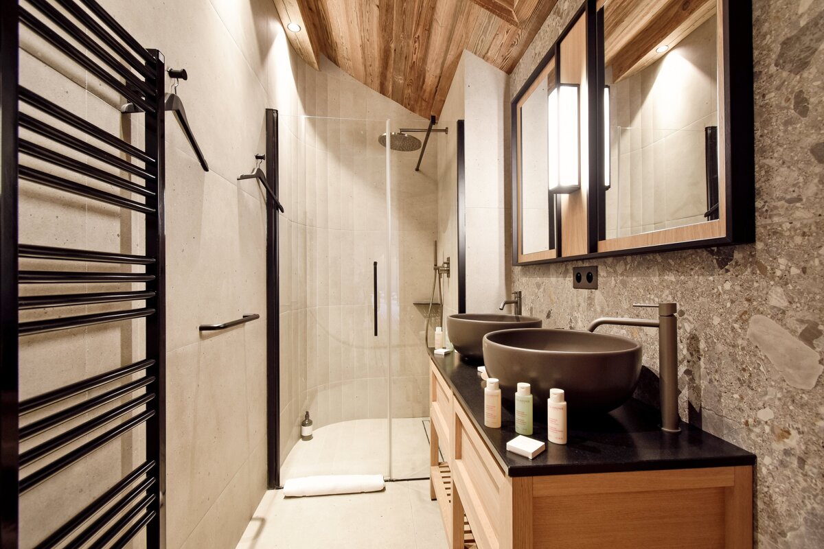Modern bathroom featuring double vessel sinks, a wooden vanity, stone walls, a glass shower, and a rustic wooden ceiling.