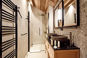 Modern bathroom featuring double vessel sinks, a wooden vanity, stone walls, a glass shower, and a rustic wooden ceiling.