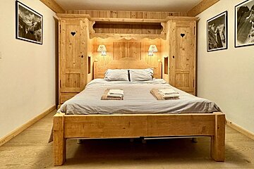 Cozy chalet-style bedroom with a light wooden bed built into matching wardrobes with heart cutouts and glowing wall lamps.