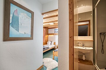 A hallway with mountain art leads to a wood-paneled twin bedroom. A bathroom with a sink and shower is visible on the right.