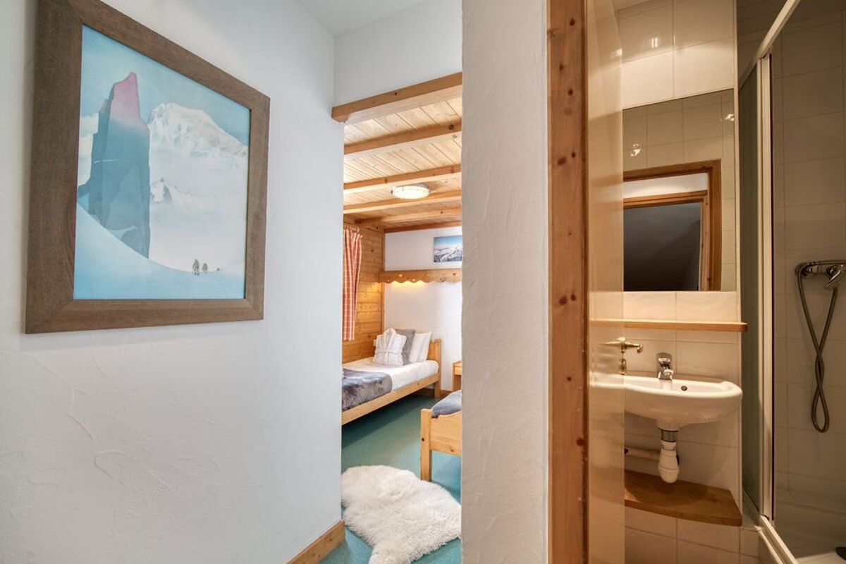 A hallway with a framed mountain picture leads to a cozy wood-paneled bedroom and a small white bathroom on the right.