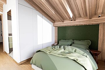 A modern bedroom with a green bed, dark green headboard, sloped wooden ceiling, and white built-in wardrobe. Sunlight illuminates the space.