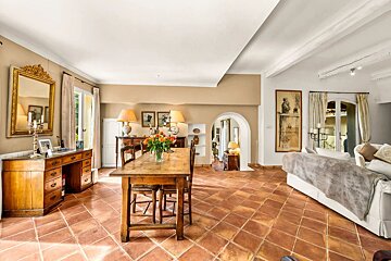 Spacious Mediterranean-style dining and living area with terracotta tiled floors, wooden furniture, and arched doorway.